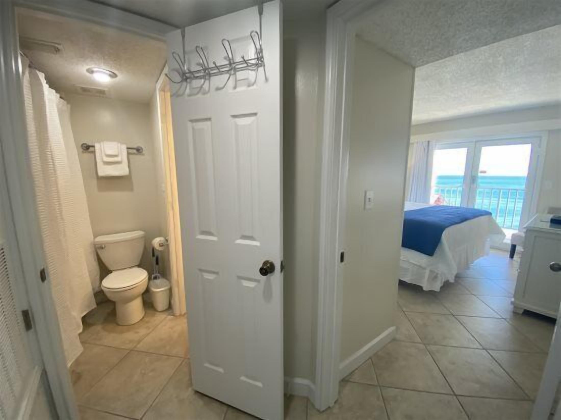 Et badeværelse med toilet, vask og bruser, samt et soveværelse med seng og balkon med udsigt.