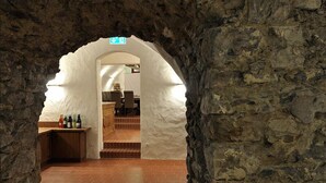 An arched doorway leading to a room with a wooden counter and bottles, a tiled floor, and a stone wall.