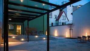 An outdoor area with a glass enclosure, steps leading to a door, and a seating area with chairs.