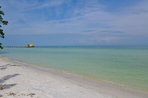 A beach with clear turquoise water, a sandy shore, and a distant building on a pier. - Ocean Pearl: *Bay front *Ground-level *Gorgeous views (Anna Maria)