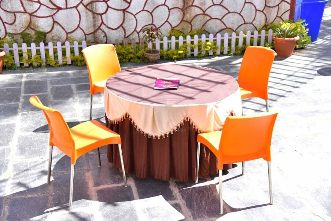 A round outdoor table with a brown tablecloth and four orange chairs.