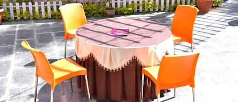 A round outdoor table with a brown tablecloth and four orange chairs.