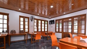 A dining area with wooden tables and orange chairs, a ceiling fan, and large windows with decorative glass panels. - Hotel Rock Villa Dalhousie (Dalhousie)