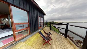 A wooden deck with a bench, a view of the water, and a building with large windows.