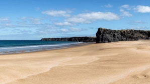 A beach with a rocky outcrop and calm sea.