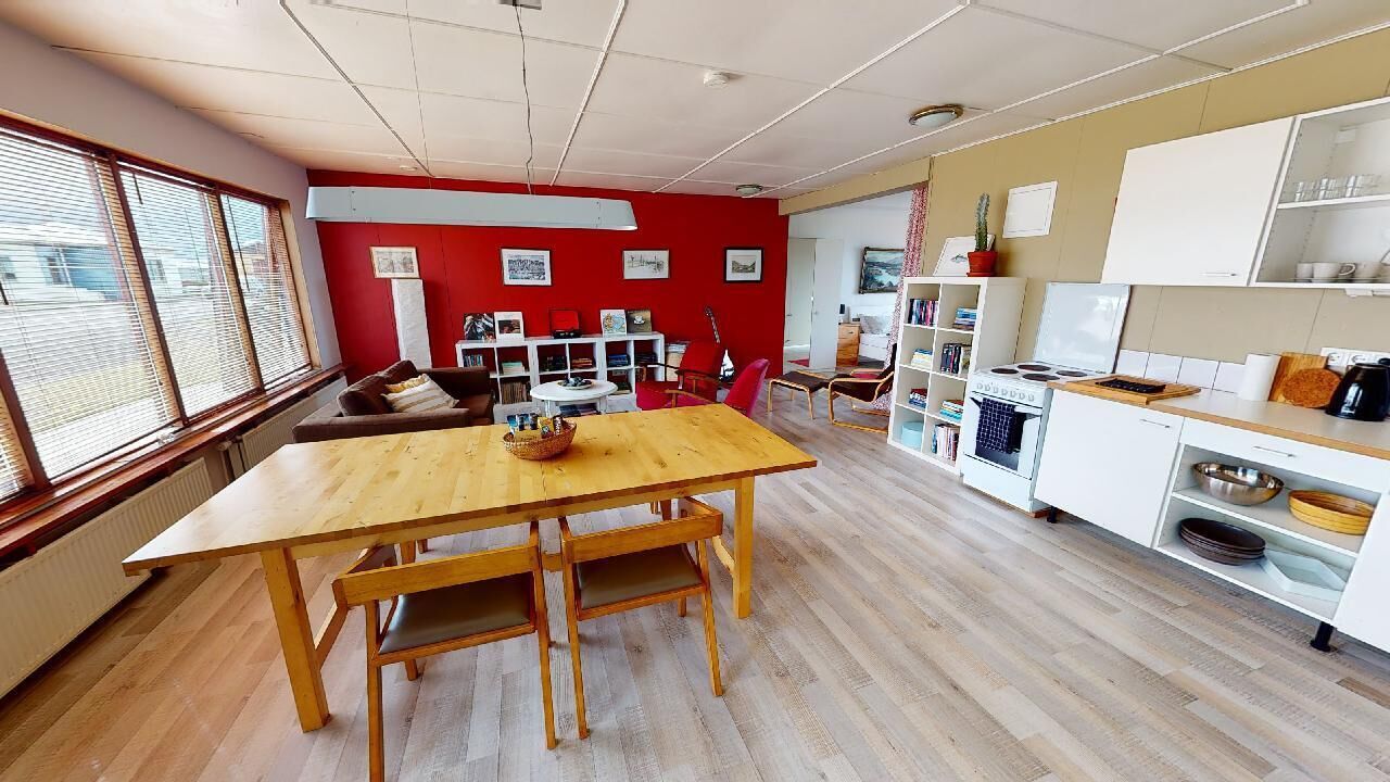 Una habitación amplia con una mesa de comedor de madera, paredes rojas y una zona de cocina con armarios blancos.