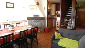 A dining area with a table and chairs, a kitchen area with a stove and cabinets, and a living room with a sofa and a staircase. - St-Lary-Soulan: Duplex T3, Sleeps 9, Fully Equipped with Balcony (Saint-Lary-Soulan)
