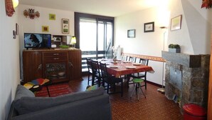 A dining area with a table set for four, a kitchen with a microwave and stove, a sofa, and a fireplace. - St-Lary-Soulan: Duplex T3, Sleeps 9, Fully Equipped with Balcony (Saint-Lary-Soulan)