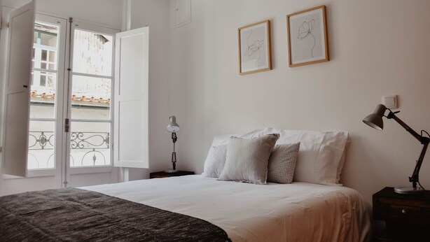 A bedroom with a bed, two bedside tables, a nightstand, a window with an open door, and two framed artworks on the wall. - Spacious, light-filled one-bedroom apartment (self check-in) (Coimbra)