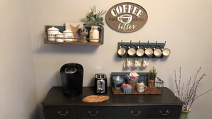 Eine Küchenarbeitsplatte mit Kaffeemaschine, Toaster und Aufbewahrungsbehältern. Darüber ein Schild mit Kaffeemotiv und eine wandmontierte Pfannendock mit Geschirr.