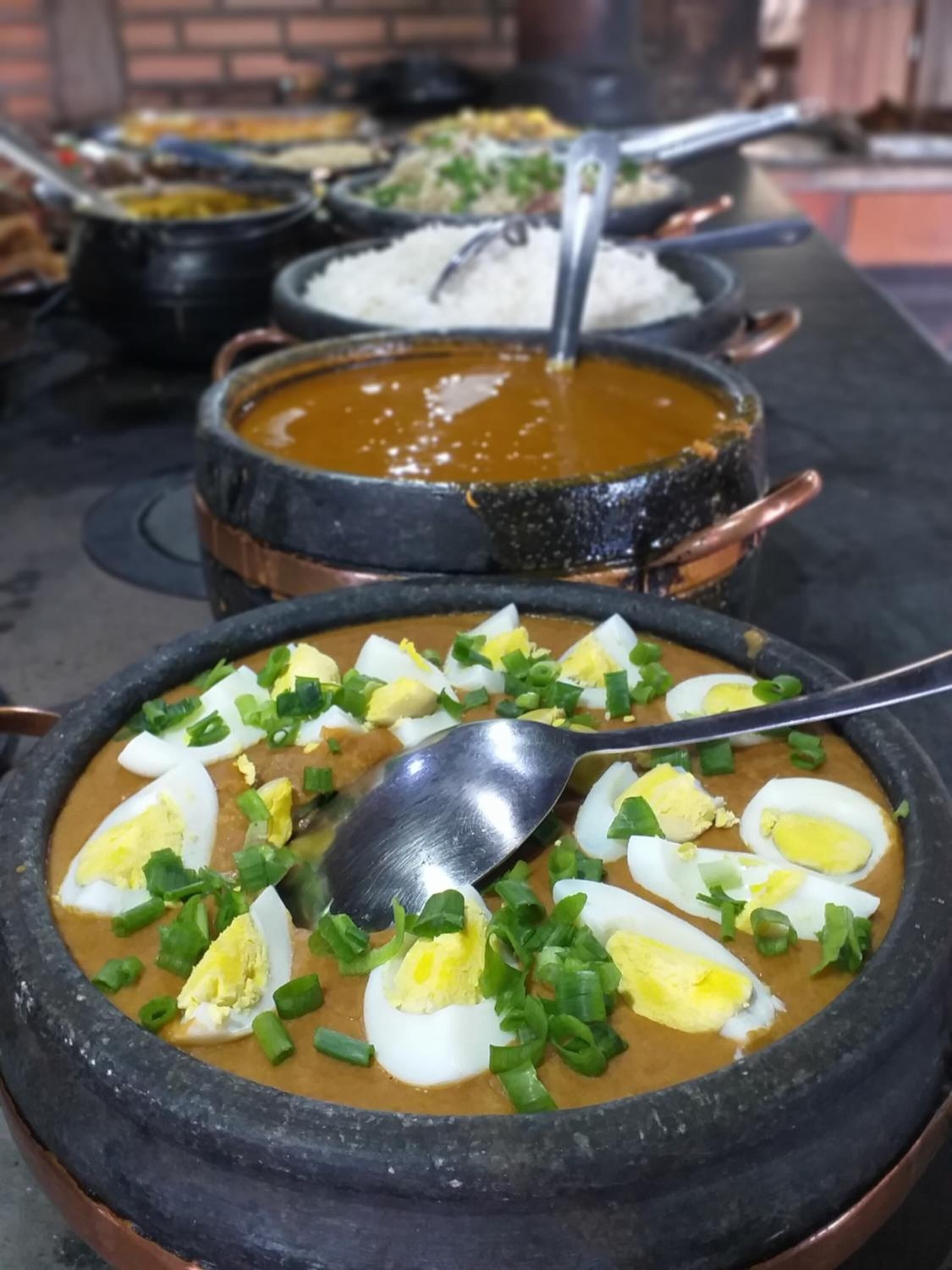Buffet com diversos pratos, incluindo uma tigela de sopa decorada com cebolinha picada e ovos cozidos.