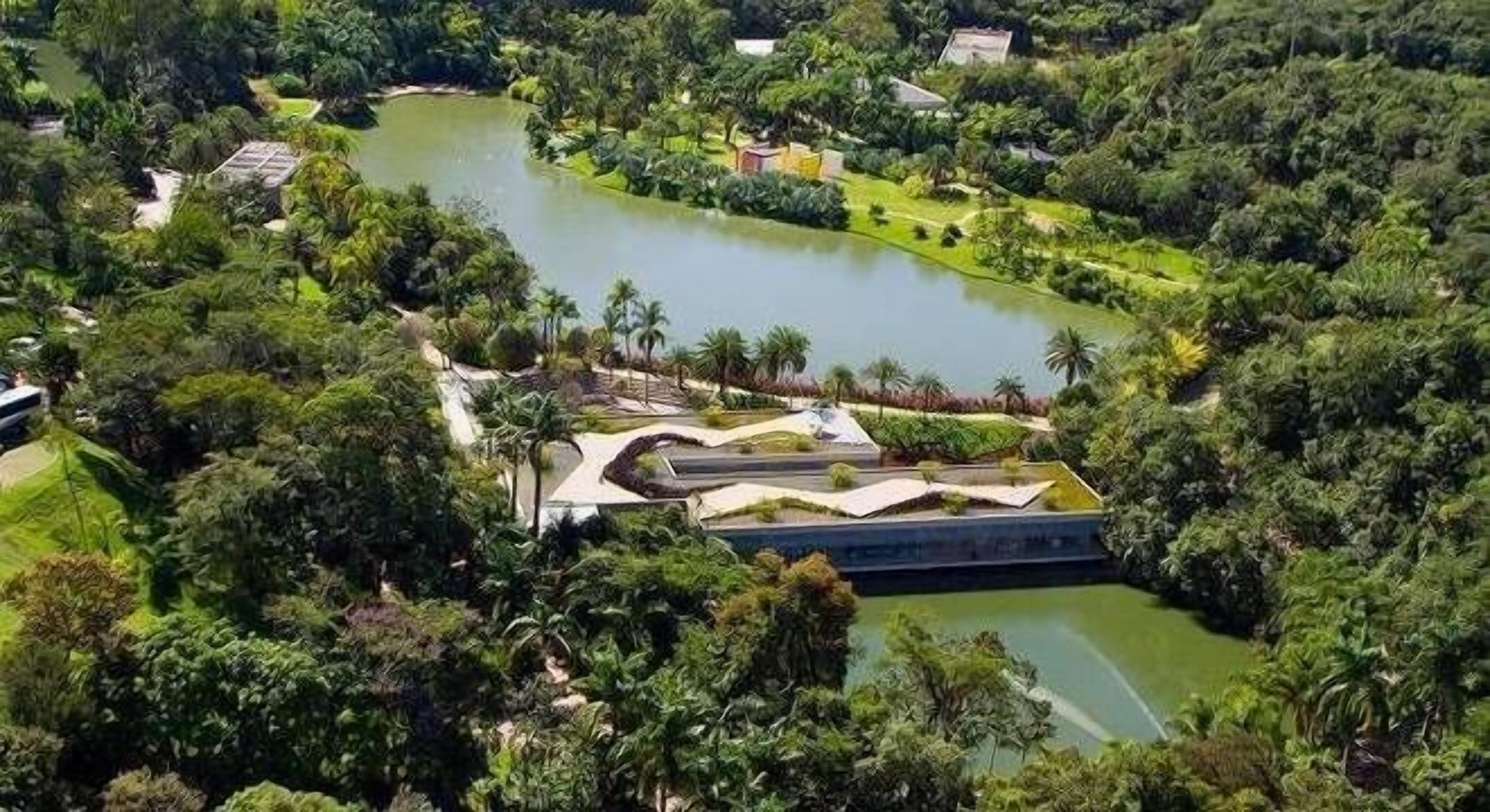 A riverside park with a bridge, lush greenery, and a small building.