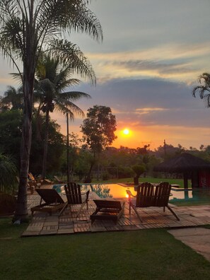 Une vue sur le coucher de soleil, avec une piscine, des chaises longues et des palmiers.
