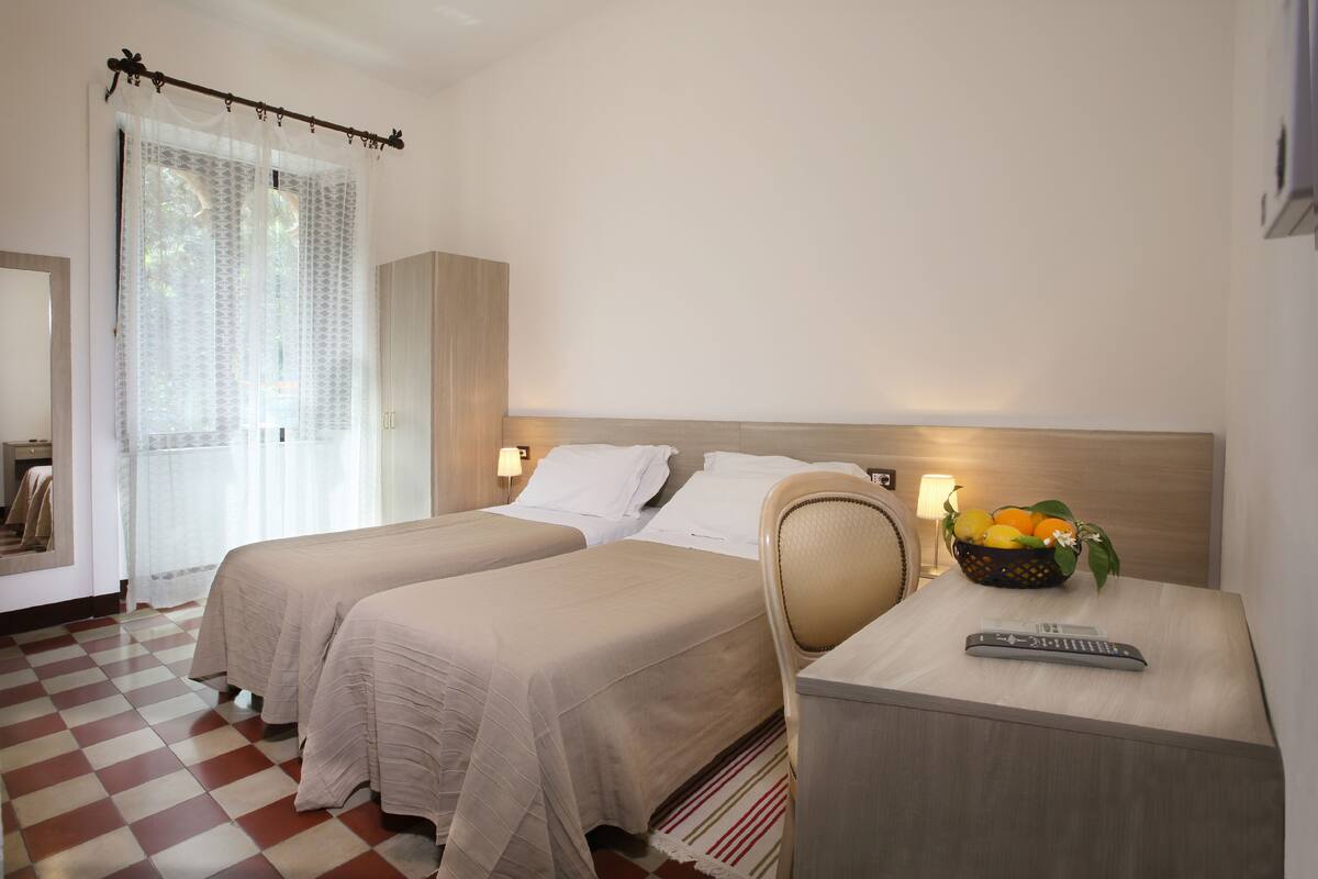 Habitación de hotel con dos camas, una mesita de noche con fruteros, un control remoto y suelo a cuadros.