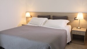 Un lit bien fait, recouvert d’une couette grise, avec deux tables de chevet dotées de lampes et une tête de lit en bois.