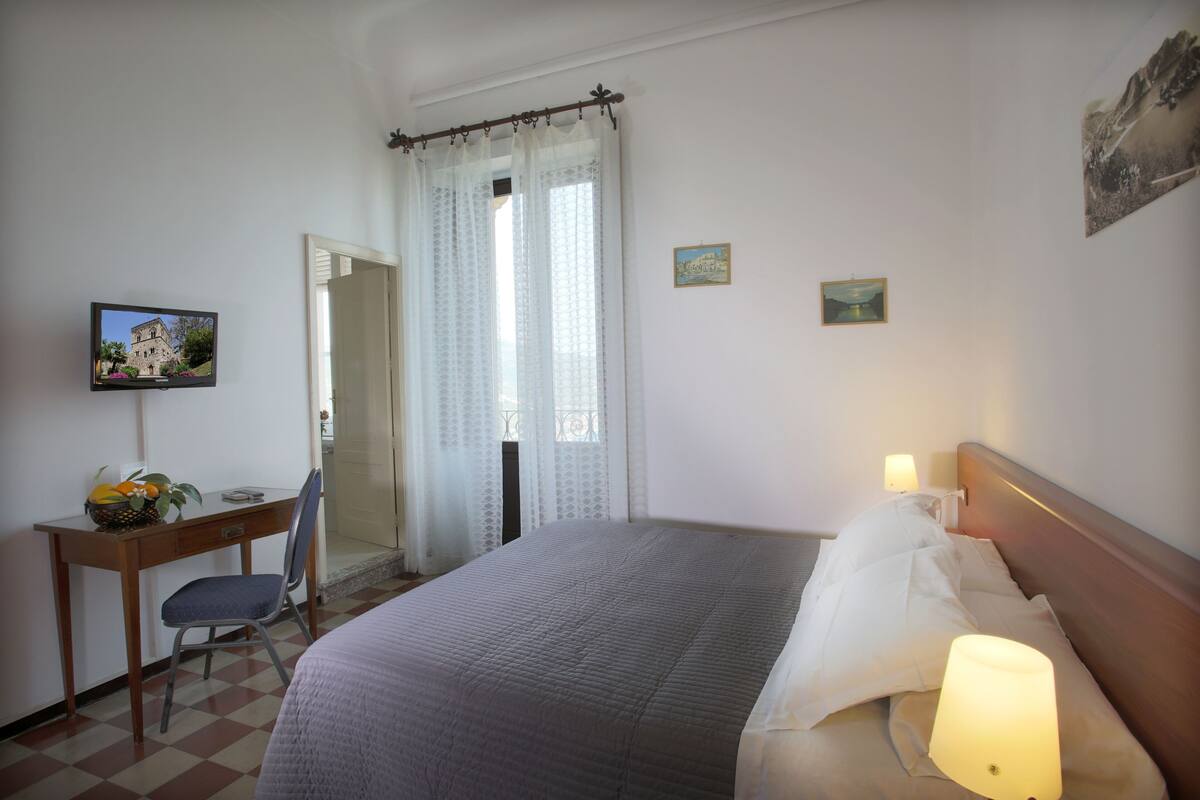 Una habitación de hotel con cama, escritorio con silla, televisor y ventana con cortinas.