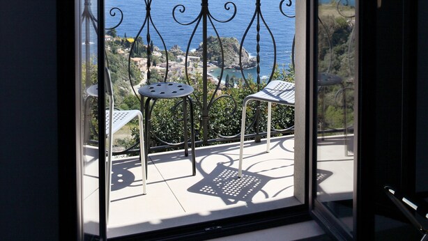 Un balcon doté d’une balustrade en métal, de deux chaises et offrant une vue sur la mer et une ville lointaine.