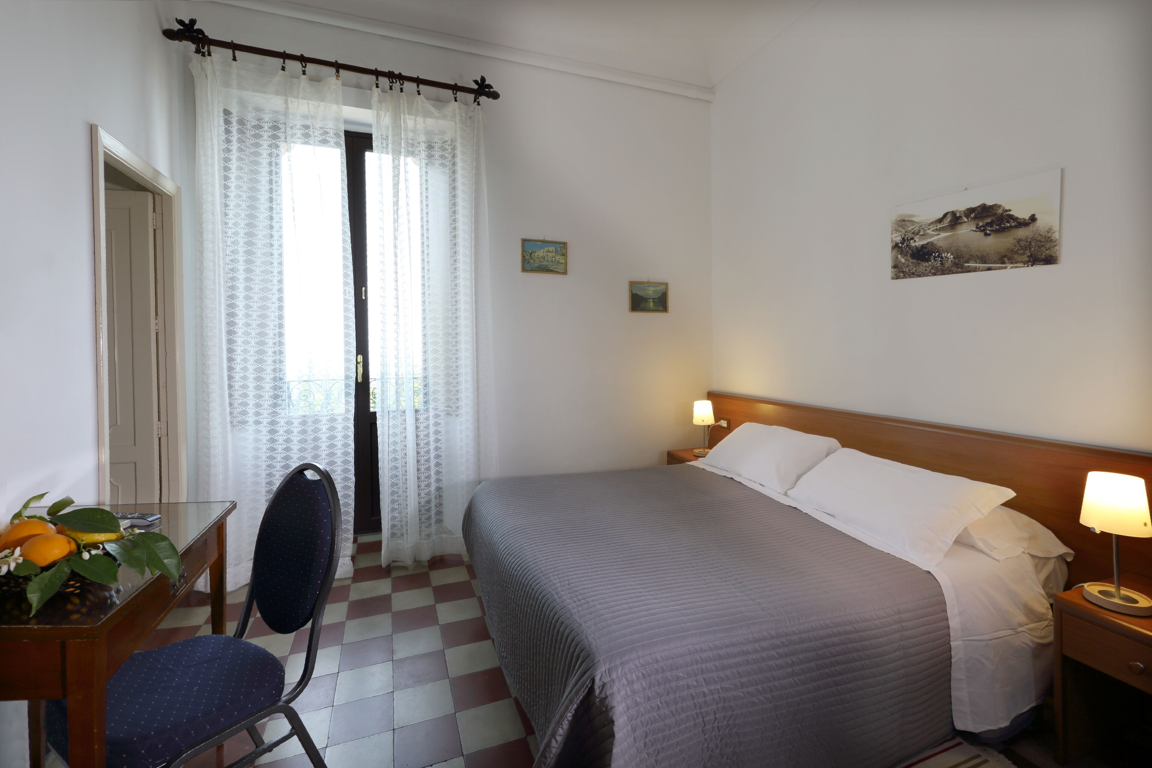 Hotelkamer met een bed, een bureau met stoel, een tafel met een plant en een raam met gordijnen.