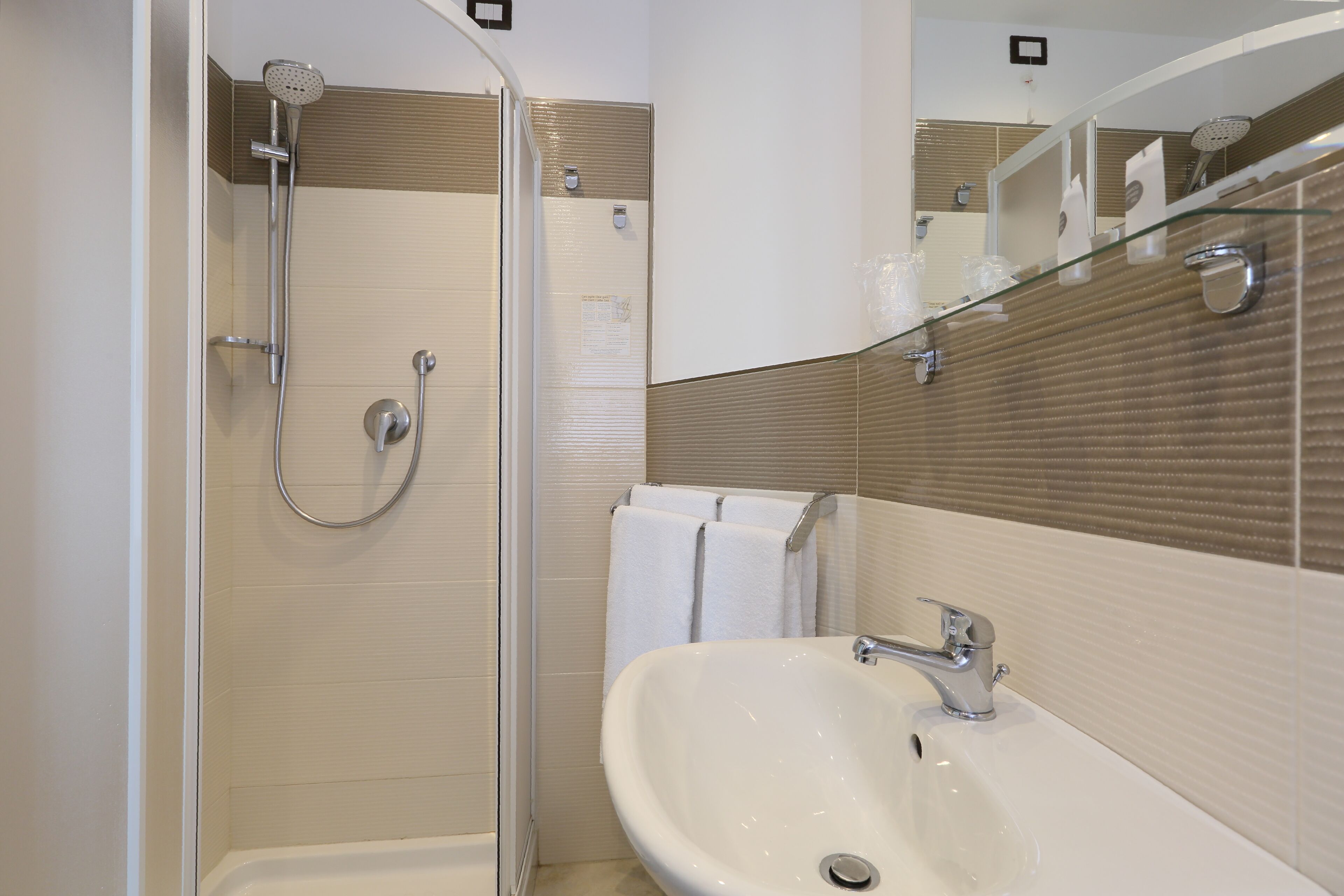 Une salle de bain moderne avec une douche à parois de verre, un lavabo blanc et un miroir doté d’une étagère en verre.