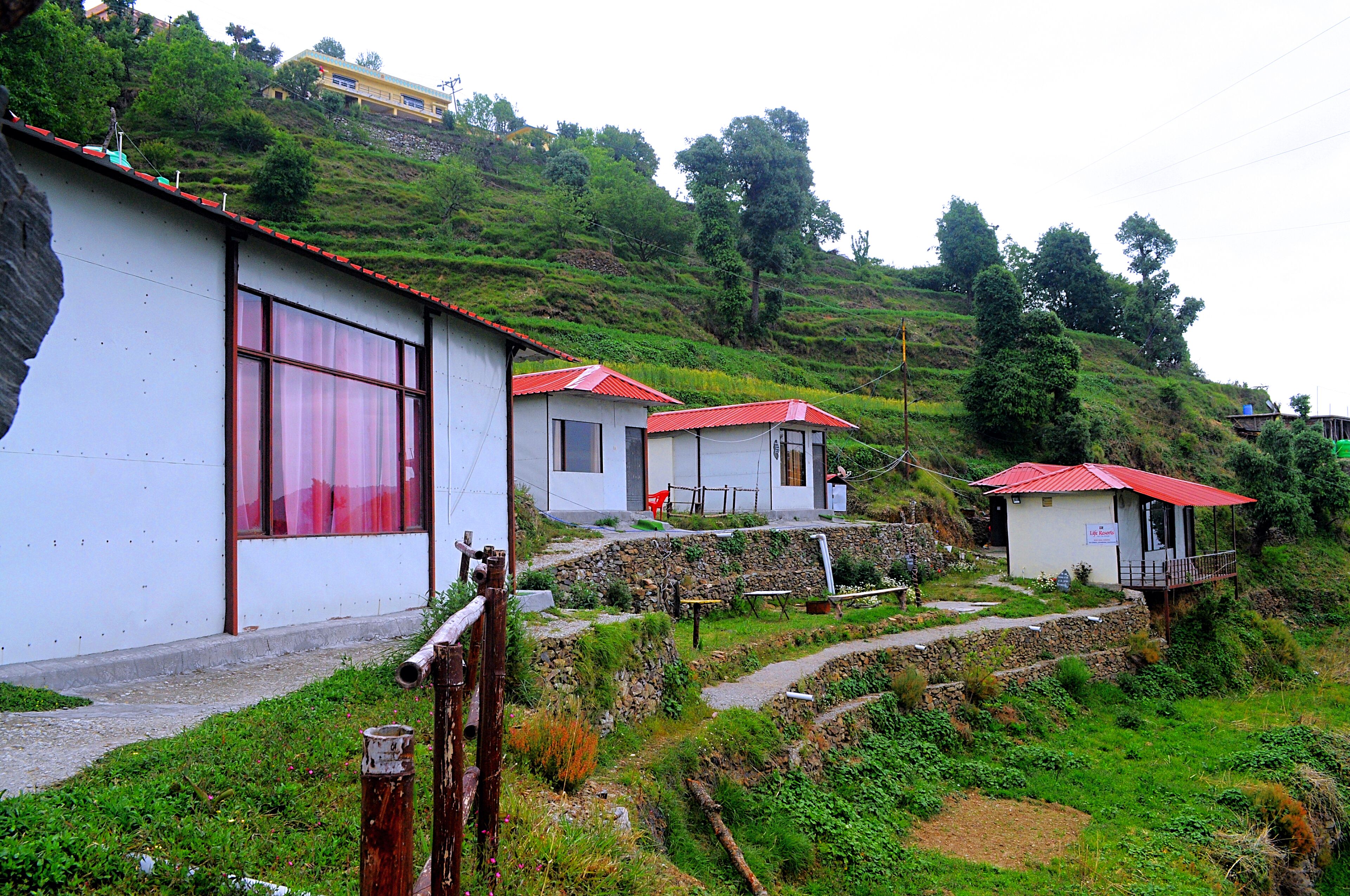 A hillside with several small buildings, each with a red roof and white walls. There are stone pathways connecting the buildings.