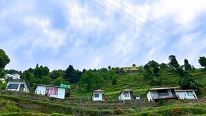 A rural landscape with several small houses on a hillside, surrounded by lush greenery and a clear sky. - Life Resorts (Tehri)