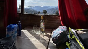 A room with a large window, red curtains, a bottle of Bacardi, two glasses, a blue water dispenser, and a backpack on a wooden table. - Life Resorts (Tehri)