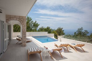A rooftop pool area with a clear view of the sea, surrounded by lounge chairs and a small table with a bowl of fruit. - Villa Nature Beauty with Heated Pool (Makarska)