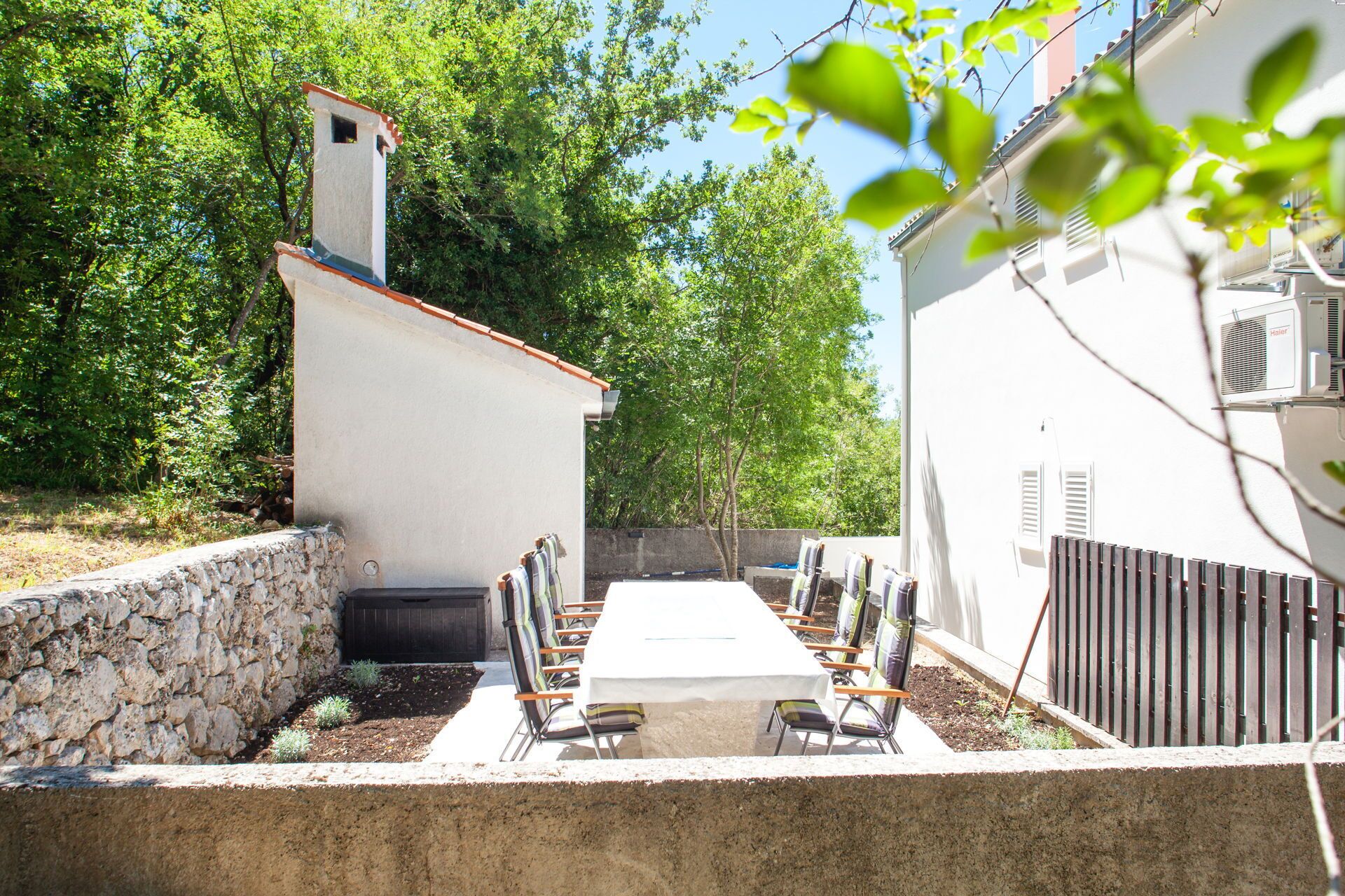 Eine Terrasse mit Tisch und Stühlen, eine Steinmauer und ein weißes Gebäude mit Schornstein.
