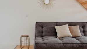 Een moderne woonkamer met een grijze bank, twee kussens, een ronde spiegel met een zonvormig frame en een klein rond tafeltje met een draadframe.