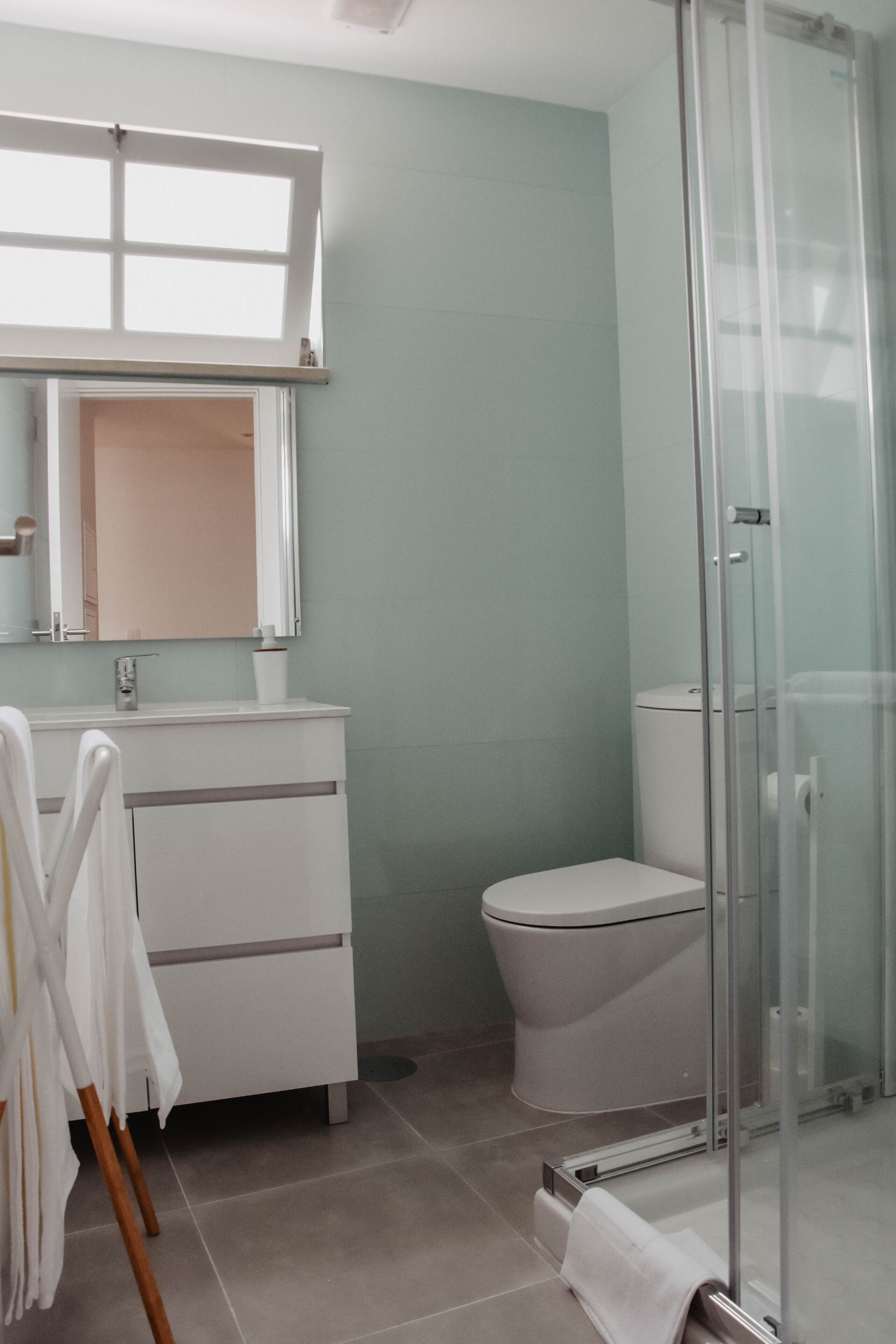 Een badkamer met toilet, een douchecabine van glas, een wit wastafelmeubel met spiegel erboven en een handdoekrek met witte handdoeken.