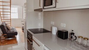 Een moderne keuken met een ingebouwde magnetron, broodrooster en koffiezetapparaat. In de aangrenzende woonruimte staat een houten ladder en een bank.