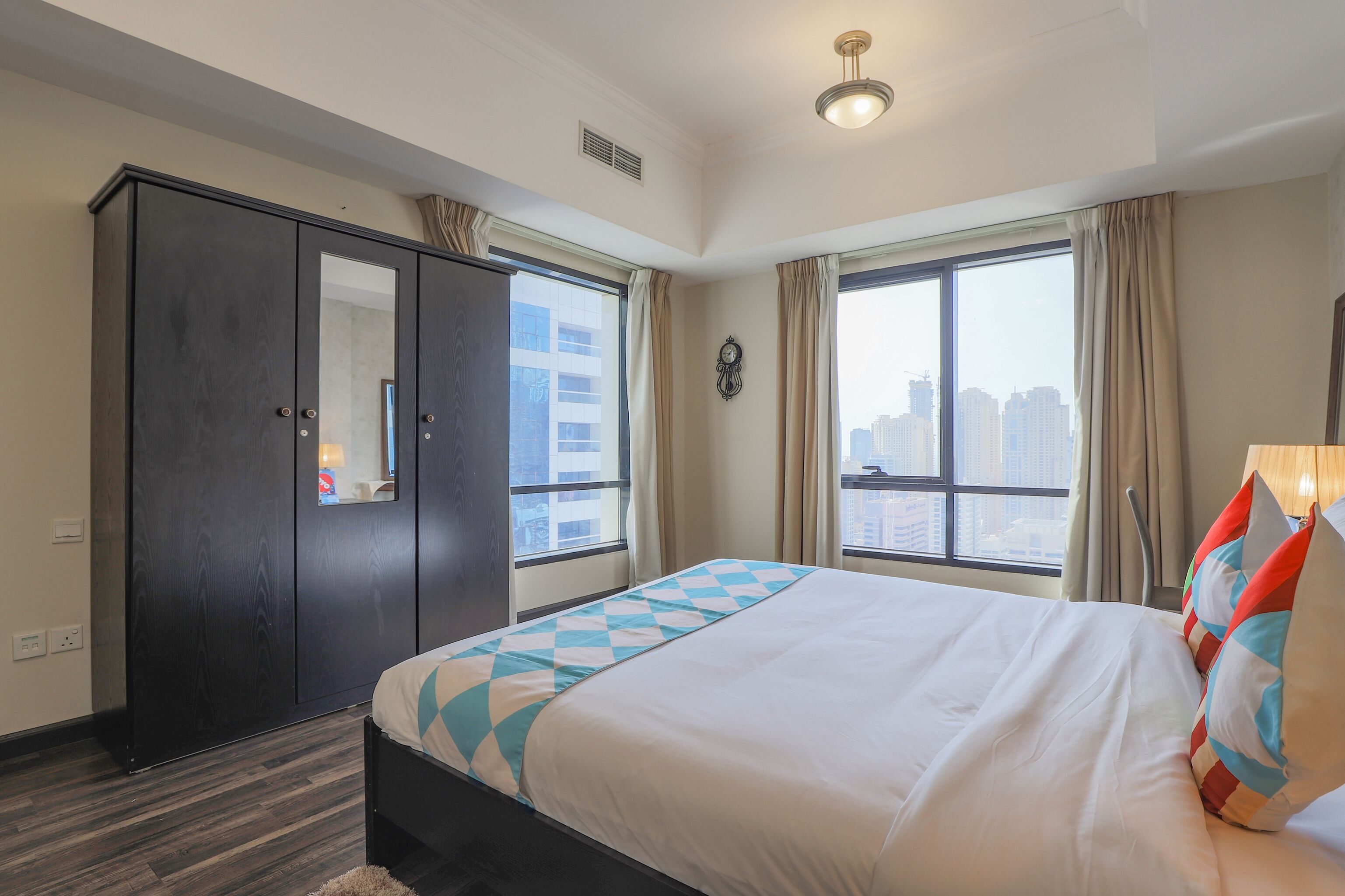 A hotel room with a large bed, a wardrobe, a window with a city view, and a ceiling light.