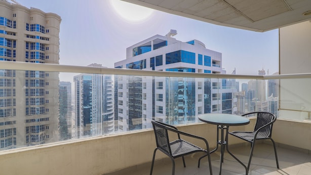 A balcony with a glass railing, two chairs, and a small table. - OYO Home 300 2BHK Al Waleed Paradise JLT (Dubai)