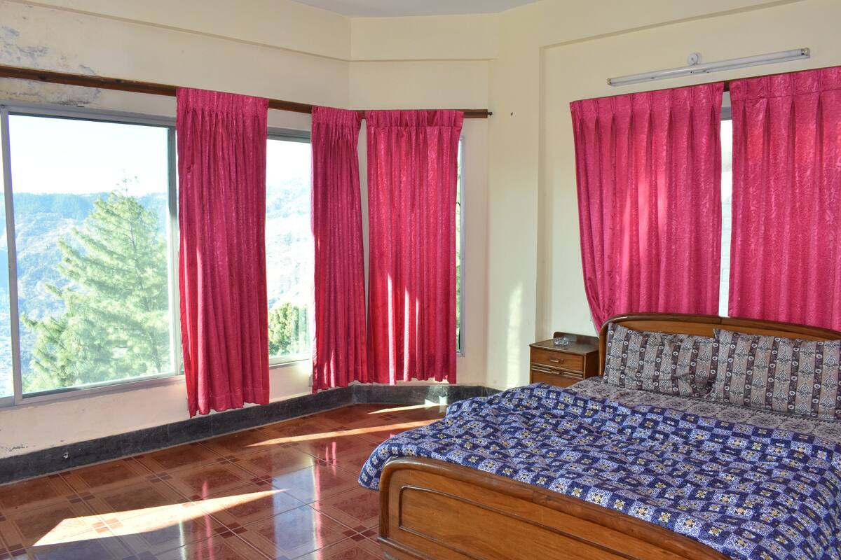 A bedroom with a wooden bed, a nightstand, and a window with red curtains.