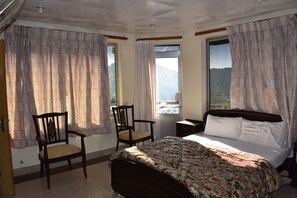 Un dormitorio con cama, dos sillas, una mesita de noche y una ventana con cortinas.