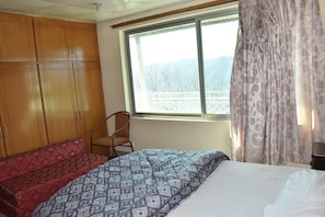 Un dormitorio con una cama, un armario de madera, una silla y una ventana con vistas a montañas.
