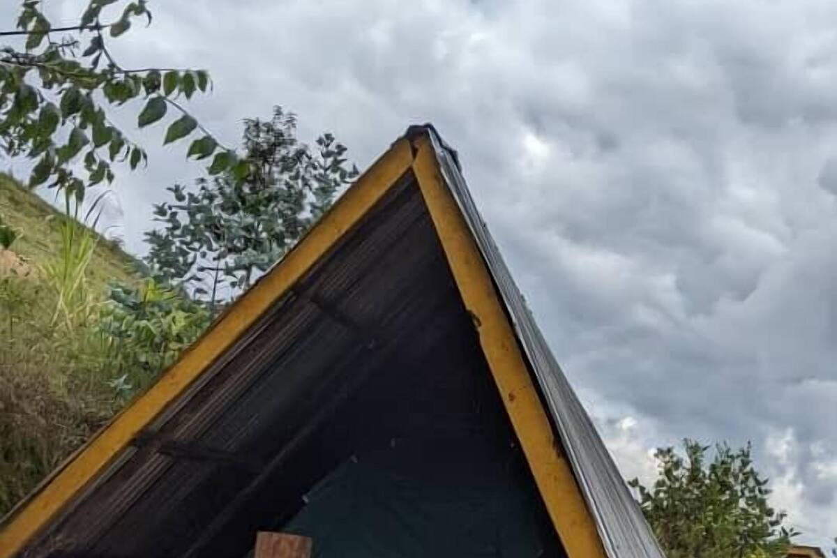 A small, triangular structure with a slanted roof, possibly a makeshift shelter or storage area, surrounded by natural vegetation and a cloudy sky.