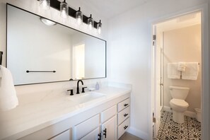 A modern bathroom with a large mirror, white vanity, black faucet, and a toilet with a patterned floor.
