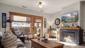 A cozy living room with a fireplace, leather sofa, and a large TV mounted on the wall. - Incredible Whitefish Mountain Ski and summer baselodge! Underground parking and close ski access (Whitefish)