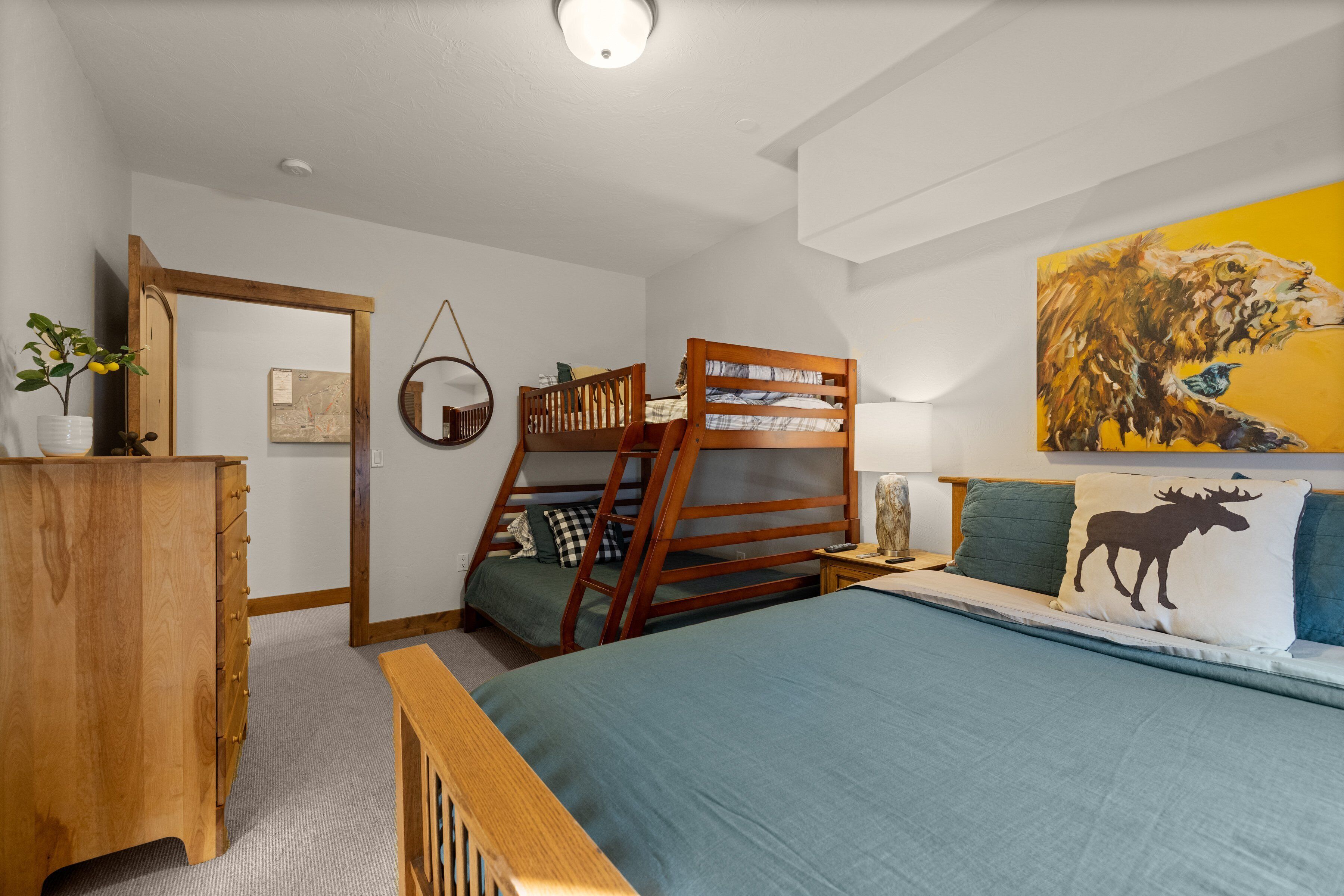Una camera da letto con un letto a castello, una cassettiera in legno, un comodino e un quadro appeso al muro.