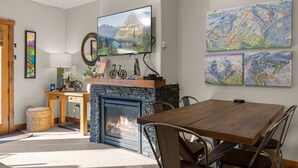 A cozy living room with a fireplace, a dining table, and a mounted TV. - Incredible Whitefish Mountain Ski and summer baselodge! Underground parking and close ski access (Whitefish)