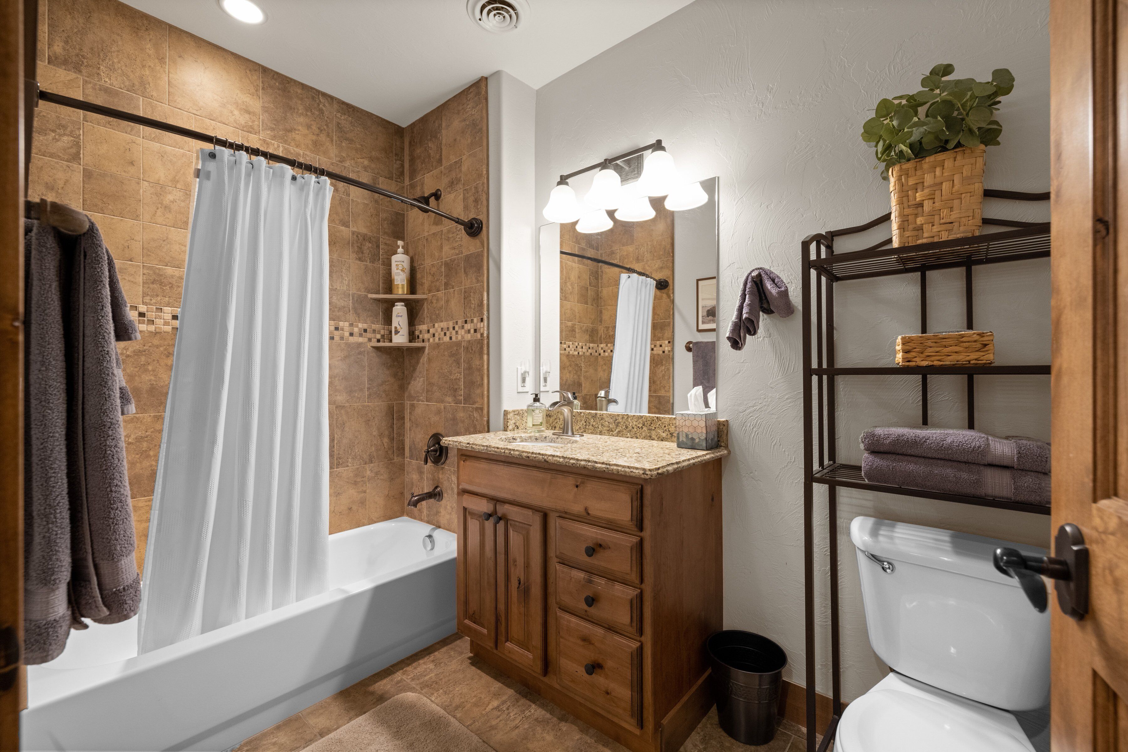 A bathroom with a bathtub, a toilet, a vanity with drawers, a mirror, and a shelf with towels.