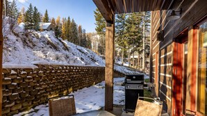 A covered outdoor seating area with a stone wall, a grill, and a view of a snowy hillside. - Incredible Whitefish Mountain Ski and summer baselodge! Underground parking and close ski access (Whitefish)