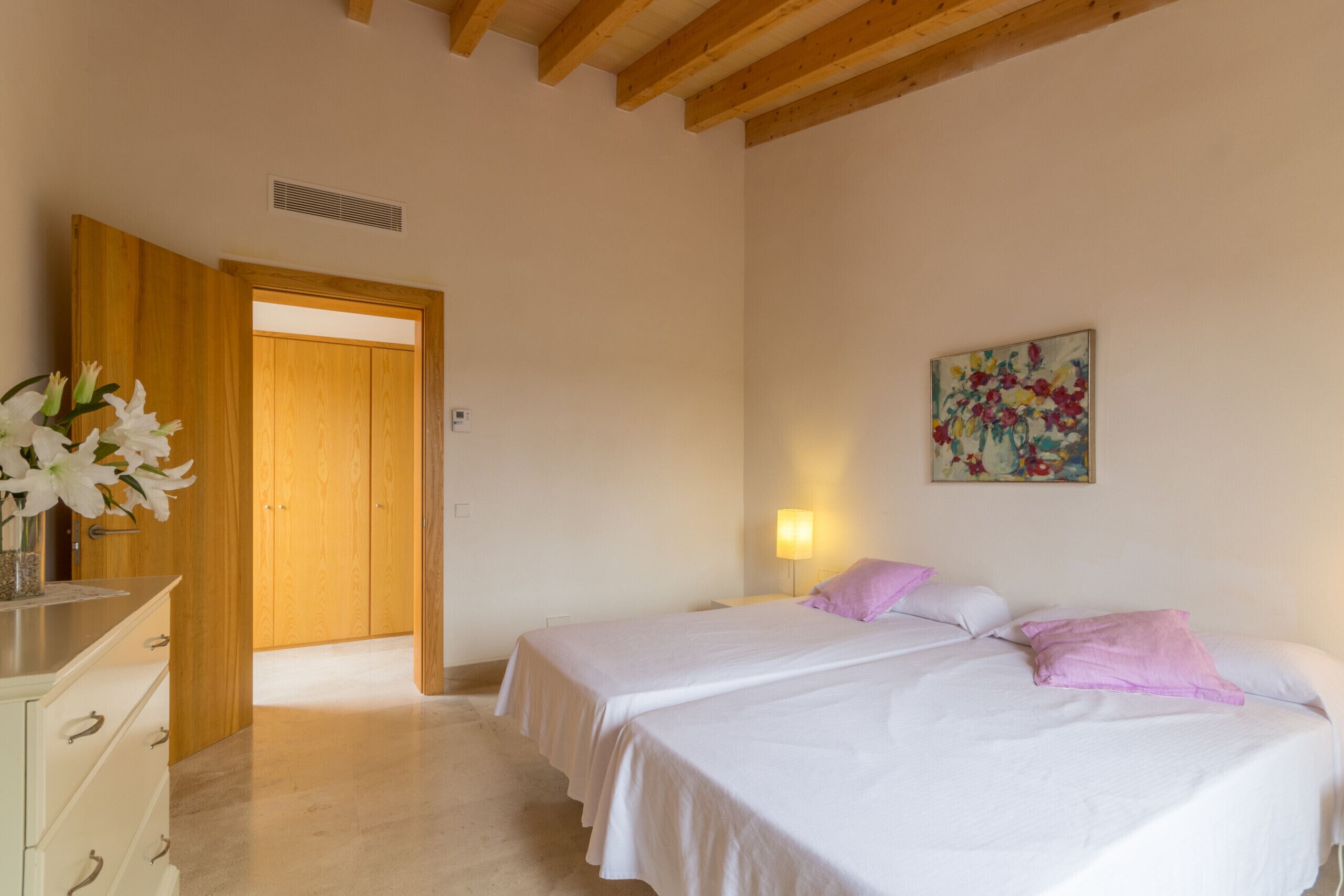 Une chambre avec deux lits, une armoire en bois, une table de chevet avec une lampe et un tableau au mur.