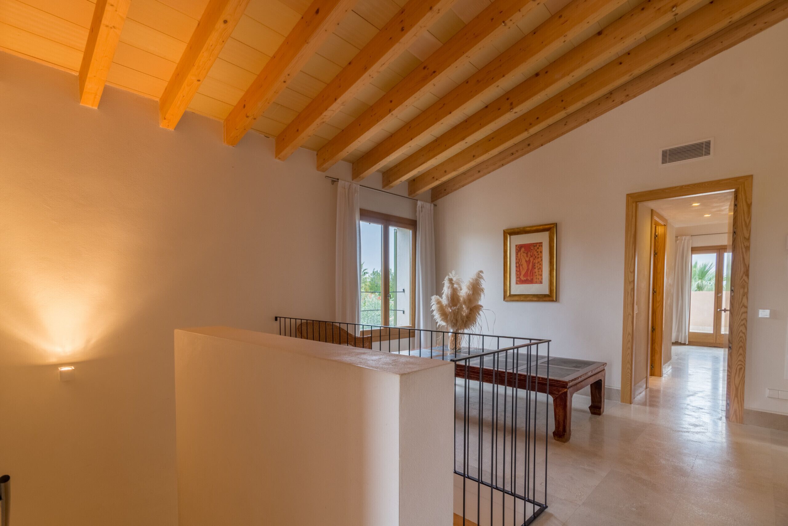 Una habitación amplia con techo alto, vigas de madera, una escalera, una mesa de comedor y vistas al exterior.