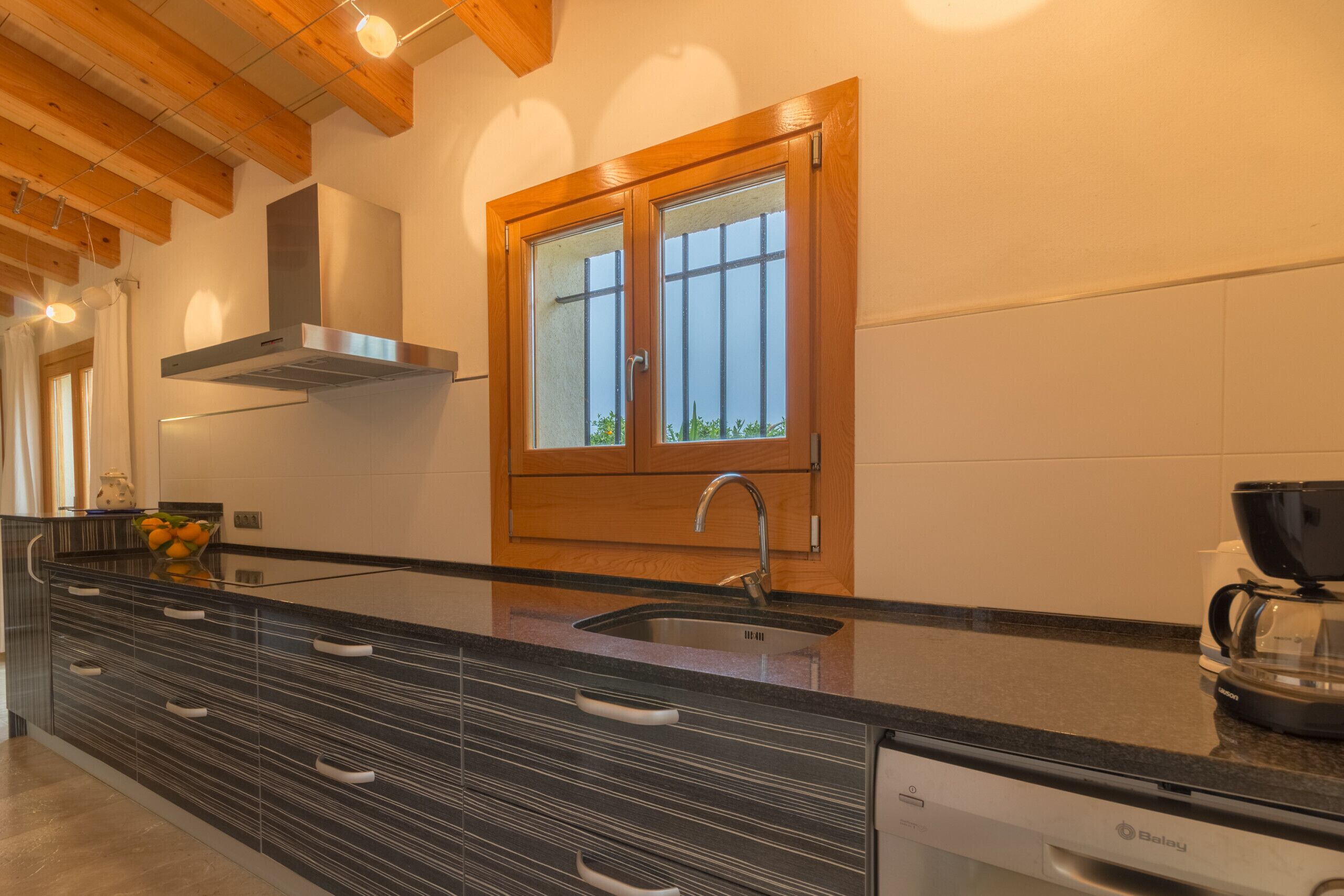 A modern kitchen with a large island, stainless steel appliances, and a window with wooden shutters.