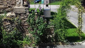 Een stenen gebouw met een rustieke uitstraling, een kleine tuin met een fontein, en een uitzicht op een groen landschap op de achtergrond.