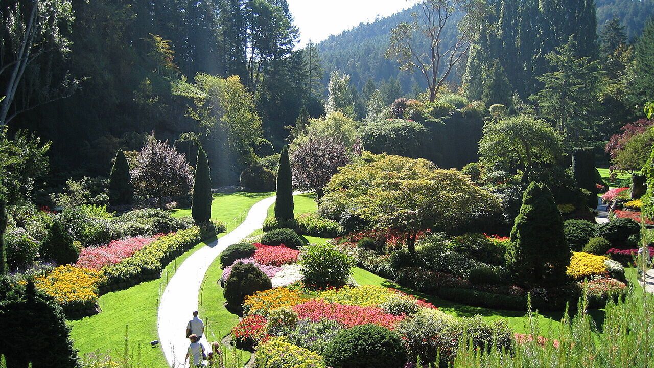 Un jardín bien cuidado con un sendero sinuoso, setos ordenados y una gran variedad de plantas en flor.