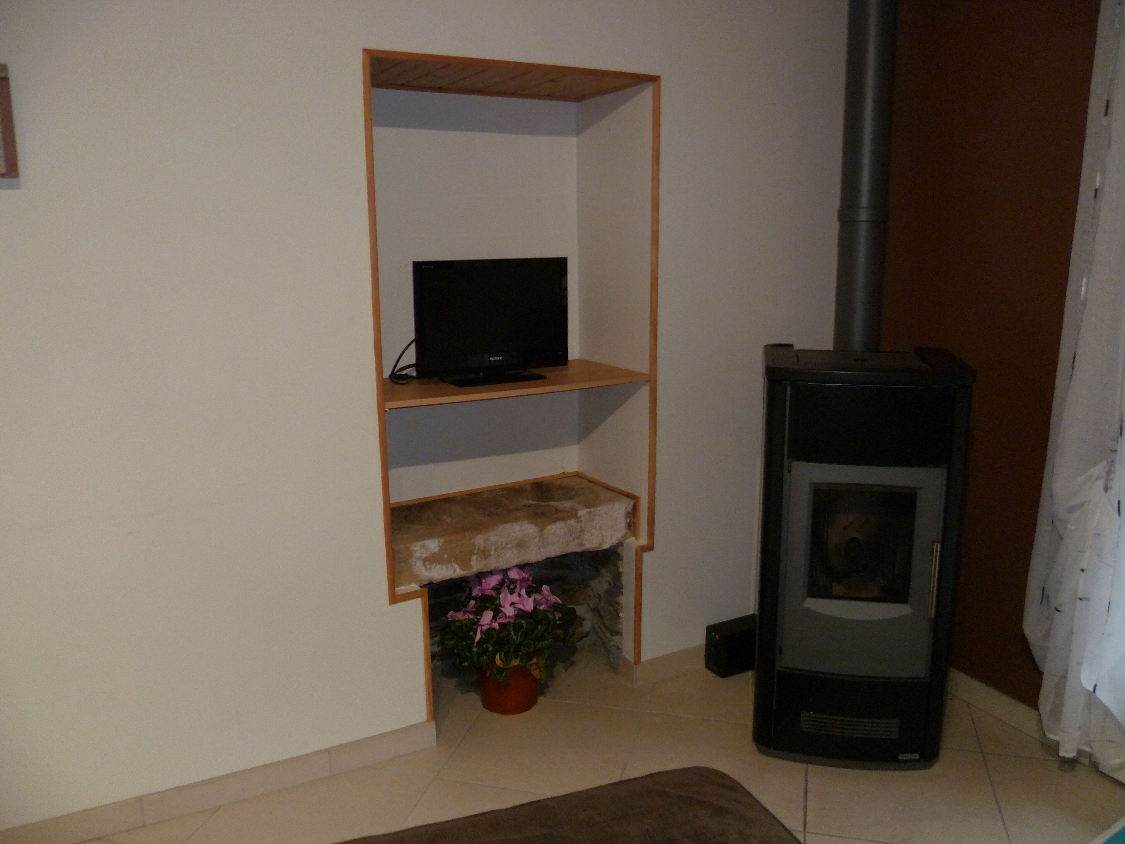 A living room with a TV on a shelf, a fireplace, and a potted plant.