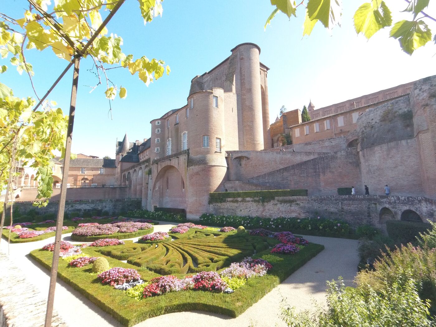 A historic building with a courtyard featuring geometric flower beds and a central fountain.